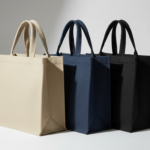 Three sturdy canvas tote bags standing in a row, featuring beige, navy blue, and black colors from left to right against a plain background.