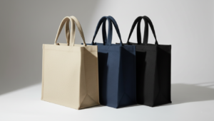 Three sturdy canvas tote bags standing in a row, featuring beige, navy blue, and black colors from left to right against a plain background.