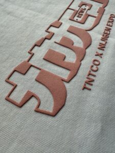 Raised high density print in salmon lettering on a grey t-shirt